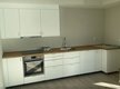 Helle, moderne Einbauküche mit weißen Schränken, Holzarbeitsplatte, Spüle und integriertem Ofen auf hellem Bodenbelag. Helle, moderne Einbauküche mit weißen Schränken, Holzarbeitsplatte, Spüle und integriertem Ofen auf hellem Bodenbelag.