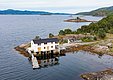 Küstenlandschaft in Hitra, Norwegen: Ein malerisches weißes Haus am Wasser, umgeben von grünen Wäldern und ruhigen Wellen, bietet eine perfekte Kulisse für Angelabenteuer und erholsame Natururlaube. Ideal für unvergessliche Angelreisen.