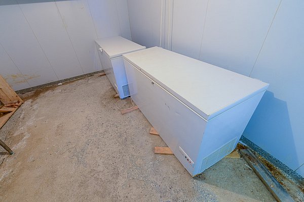 Zwei weiße Gefriertruhen stehen in einem einfachen, fensterlosen Raum mit Betonboden und weißen Wänden. Ideal für die Lagerung großer Fischfänge während deines Angelurlaubs in Nordland, Norwegen.