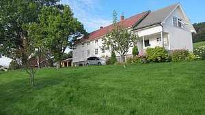 Weißes, traditionelles Haus in Hitra, Norwegen, umgeben von grüner Wiese und blühenden Bäumen. Ideal für Ruhe und Angelabenteuer. Skandinavische Landschaft, die zur Entspannung und Entdeckung einlädt. Perfekt für Angelreisen und Naturerlebnisse.