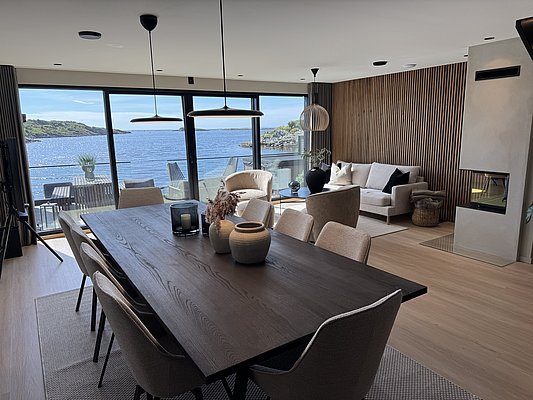 Moderne skandinavische Ferienwohnung mit Panoramafenstern, die einen atemberaubenden Blick auf die Küstenlandschaft Südwest-Norwegens bieten. Stilvolles Interieur mit Holztönen und Kamin laden zur Entspannung nach einem Angelabenteuer ein. Ideal für Angelreisen.
