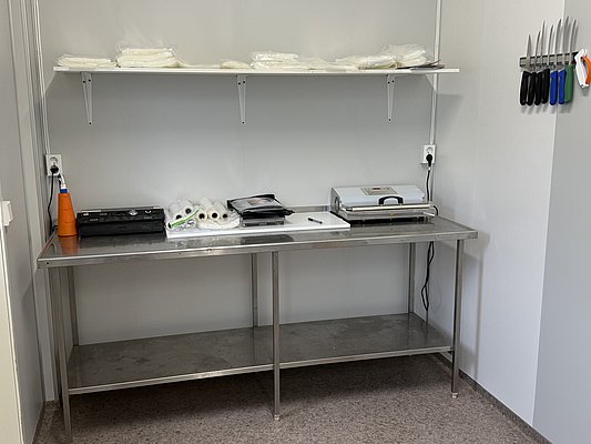 Arbeitsbereich zur Fischverarbeitung in Nord-Norwegen, ausgestattet mit Messerhalter, Vakuumgerät und Rollen für Frischhaltefolie, ideal für vorbereitende Angelurlaube und das Meeresangeln in Skandinavien. Perfekt für einen erfolgreichen Angelurlaub.
