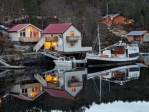 Gemütliche Fischerhütten mit roten Dächern am ruhigen Wasser bei Hitra, Norwegen. Zwei Boote liegen im klaren Fjord, perfekt für Angelabenteuer und Erholung in malerischer Natur.