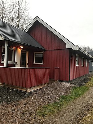 Rote Holzhütte auf Hitra, Norwegen. Ideal für Angelurlaub, umgeben von malerischer Natur. Einladende Veranda, perfekter Ausgangspunkt für Meeresangeln und Erholung in skandinavischer Landschaft.