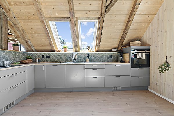 Gemütliche Dachküche in Südwest-Norwegen mit Holzakzenten, Dachfenstern und moderner Ausstattung. Helle Holzdecke und stilvolle, graue Küchenschränke schaffen eine einladende Atmosphäre. Ideal für entspanntes Kochen nach einem erfolgreichen Angeltag.