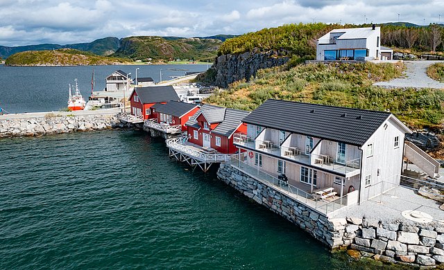 Gemütliche rote Holzhäuser am Wasser in Hitra, Norwegen, umgeben von üppiger Landschaft. Perfekter Ausgangspunkt für Angelabenteuer und Erholung am Meer. Ruhige Atmosphäre und atemberaubende Aussicht bieten ideale Bedingungen für unvergessliche Angelreisen.