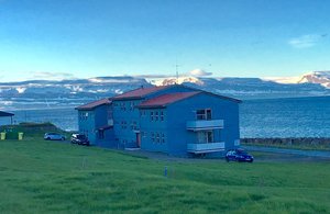 Blaue Gebäude nahe Sudavik, Island, mit Blick auf verschneite Berge und das Meer. Ideal für Angelurlauber, die Abenteuer und Ruhe kombinieren möchten. Perfekte Kulisse für Naturliebhaber und Erholung in einer malerischen Umgebung.