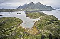 Luftaufnahme der idyllischen Küstenlandschaft in Nordland, Norwegen: grüne Inseln, stilles Wasser, Berge im Hintergrund, kleine Anlegestelle mit Booten. Ideal für naturverbundene Angelreisen und entspannende Abenteuerferien.