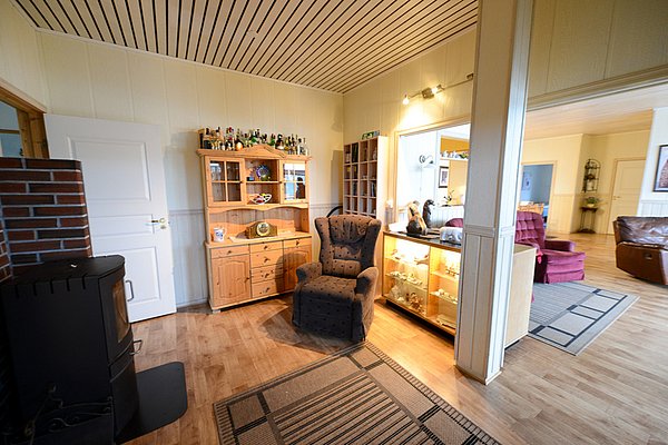 Gemütliches Wohnzimmer in Nord-Norwegen mit Holzmöbeln, Kamin und Vitrine. Ideal zum Entspannen nach einem erlebnisreichen Angelurlaub. Helle und einladende Atmosphäre für erholsame Stunden in skandinavischem Ambiente.