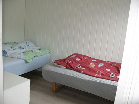 Gemütliches Schlafzimmer in Nordland, Norwegen, mit zwei Einzelbetten und bunten Decken. Helle Holzwände und ein schlichter Boden sorgen für eine einladende Atmosphäre, ideal für Angler auf Reisen.