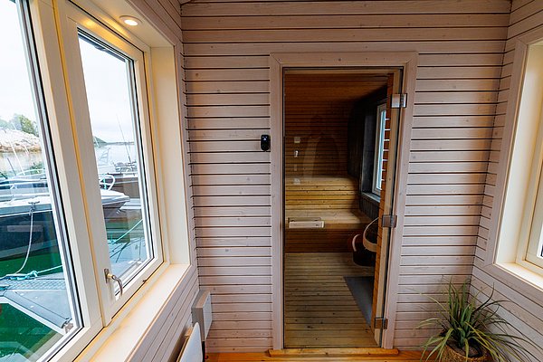 Gemütlicher Innenbereich in Nordland, Norwegen: Eine Sauna mit Holzwänden und Glasfront lädt zur Entspannung ein. Große Fenster bieten Ausblick auf Boote und Wasser, verstärken maritimes Flair. Perfekt für erholsamen Angelurlaub.