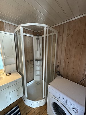 Duschbereich mit Waschmaschine in gemütlicher Holzhütte in Hitra, Norwegen. Ideal für Angelreisende, die Komfort und Praktikabilität schätzen. Perfekter Rückzugsort nach einem aufregenden Tag beim Meeresangeln.