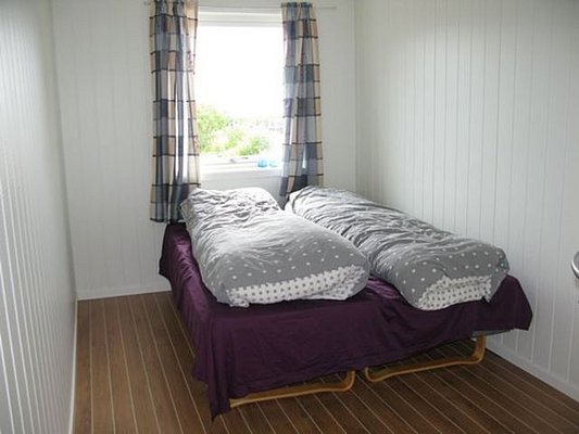Gemütliches Schlafzimmer in Nordland, Norwegen, mit zwei Einzelbetten, Holzboden und Fenster mit Blick auf grüne Landschaft. Perfekte Unterkunft für Angelurlauber, die Entspannung und Abenteuer kombinieren möchten.