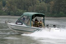 Ein Fischereiboot mit mehreren Anglern fährt auf einem Fluss, umgeben von dichter Waldlandschaft.
