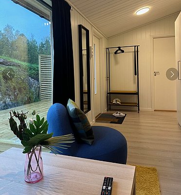 Gemütlich eingerichtetes Zimmer in Hitra, Norwegen, mit modernem Dekor, bequemer Sitzgelegenheit und großem Fenster, das den Blick ins Grüne freigibt. Ideal für entspannte Angelurlaube in natürlicher Umgebung.