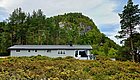 Hütte in Hitra, Norwegen, umgeben von grünen Nadelbäumen und hügeliger Landschaft. Ideal für Angelurlaub und Naturerlebnisse. Malerische Kulisse für Erholung und Abenteuer inmitten üppiger Vegetation und friedlicher Umgebung.