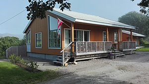 Gemütliches Holzhaus in Hitra, Norwegen, mit Veranda und norwegischer Flagge. Ideal für Angelreisen in malerischer Umgebung. Perfekt zum Entspannen und Natur genießen. Angelurlaub im skandinavischen Stil erleben. Barrierefreiheit: Stufen am Eingang.