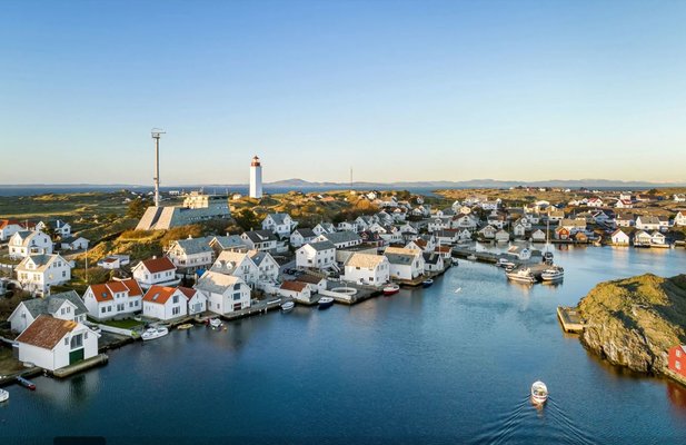 Luftaufnahme eines malerischen Küstendorfs mit weißen Häusern, einem Leuchtturm und mehreren Booten im ruhigen blauen Wasser. Luftaufnahme eines malerischen Küstendorfs mit weißen Häusern, einem Leuchtturm und mehreren Booten im ruhigen blauen Wasser.