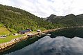 Hütte an bewaldeter Küste in Nord-Norwegen, umgeben von Bergen und ruhigem Wasser. Perfekter Ort für Angelurlaub und Naturerlebnisse. Klarer Himmel spiegelt sich im Fjord. Entspannende, idyllische Landschaft für Abenteurer.