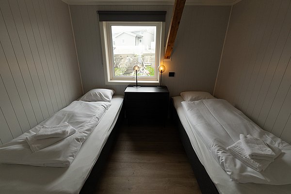 Kompaktes Schlafzimmer in Nordland, Norwegen, mit zwei Einzelbetten, modernem Design und Holzdekor. Ein Fenster bietet Ausblick auf ruhige Umgebung. Ideal für entspannende Angelreisen und erholsame Übernachtungen.