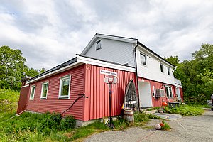 Rotes und weißes Haus in Nord-Norwegen mit Basketballkorb im Vorgarten. Umgeben von grüner Landschaft, vermittelt es ländliche Idylle und Entspannungsmöglichkeiten. Perfekt für Angelurlaub und Erkundungen in der Natur.