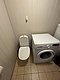 Waschraum in Hitra, Norwegen: Moderne Waschmaschine neben einer Toilette auf hellen Fliesen. Funktionale Ausstattung für Reisende, die Komfort und Praktikabilität in ihrer Unterkunft suchen. Ideal für Angelreisende in Norwegen.