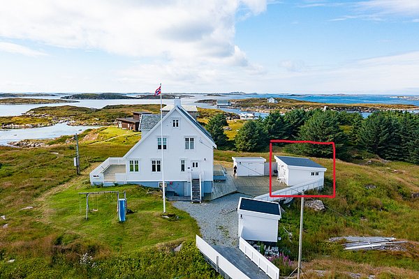 Küstenlandschaft in Hitra, Norwegen: Ein weißes Haus mit norwegischer Flagge, umgeben von üppiger Natur und Blick auf das Meer, ideal für Angelreisen und Naturerlebnisse. Perfekt für deinen nächsten Angelurlaub.