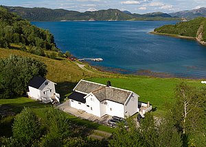 Luftaufnahme von Hitra, Norwegen: Weiße Häuser in grüner Landschaft am blauen Fjord. Ideal für Angelurlaub mit toller Aussicht. Perfekte Kombination aus Natur und Erholung.