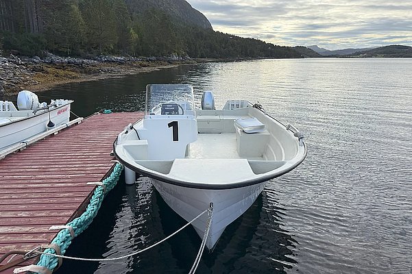 Ein einsames weißes Angelboot liegt vertäut an einem hölzernen Steg am malerischen Ufer von Hitra, Norwegen, umgeben von stiller, ruhiger Natur. Perfekter Ausgangspunkt für Angelreisen und Erkundungen.