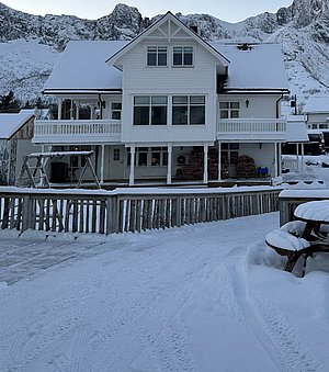 Winterliches Holzhaus in Nord-Norwegen, umgeben von schneebedeckten Bergen. Skandinavische Architektur mit verschneiten Dächern. Perfekt für Angelreisen und Naturerlebnisse in ruhiger, idyllischer Landschaft. Idealer Ausgangspunkt für Abenteuer und Erkundungen.