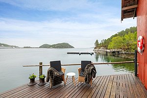 Gemütliche Terrasse in Hitra, Norwegen, mit Blick auf ruhiges Wasser und bewaldete Inseln. Zwei Stühle mit Decken laden zum Entspannen ein. Perfekte Kulisse für erholsamen Angelurlaub und Naturgenuss.