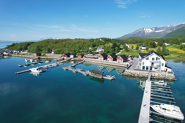 Klares Wasser in Nord-Norwegen: Malerischer Hafen mit roten Holzhäusern, Bootsanlegestellen und beeindruckenden Bergen im Hintergrund. Perfektes Angelurlaubsziel in skandinavischer Naturidylle.