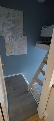 Kleiner, einfacher Raum in Nordland, Norwegen mit Holzleiter zu Hochbett, maritimer Wandkarte und schlichtem Holzboden. Perfekt für minimalistische Übernachtungen während des Angelurlaubs.