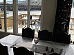 Innenansicht eines Wohnzimmers in Nordland, Norwegen: Blick durch große Fenster auf eine sonnige Holzterrasse mit Tisch am Wasser, umgeben von felsiger Landschaft. Perfekte Kulisse für Angelabenteuer und Entspannung.