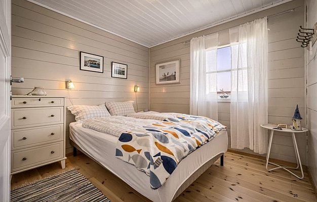 Gemütliches Schlafzimmer in Südwest-Norwegen. Helles, skandinavisches Design mit Holzwänden, Doppelbett, dekorativen Bildern, Matratzen und Kissen. Ideal für erholsame Angelurlaube in der Region. Sonnenlicht durchflutet den Raum durch ein großes Fenster.