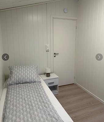 Einladendes Einzelzimmer in Hitra, Norwegen, mit hellem Holzinterieur. Gemütliche Bettwäsche und Nachttischlampe bieten Komfort für Angelreisende. Ideal für erholsame Nächte nach einem Tag voller Abenteuer.