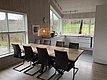 Moderne Küche in Hitra, Norwegen, mit großem Esstisch, stilvollen Stühlen und Panoramafenstern. Helle Holzakzente und eine Hängeleuchte schaffen eine gemütliche Atmosphäre. Ideal für Angelreisende, die Komfort und Natur verbinden möchten.
