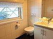 Modernes, gefliestes Badezimmer in Nord-Norwegen, kombiniert Funktionalität und Stil. Helles Tageslicht durch das Fenster, elegante Sanitärkeramik und frische Handtücher schaffen eine komfortable Atmosphäre nach einem langen Angeltag. Perfekt für erholsame Momente.