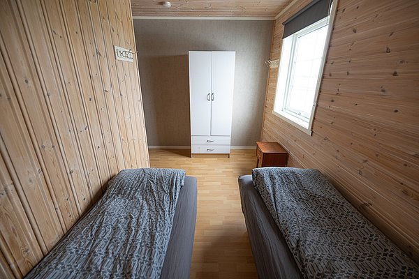 Gemütliches Schlafzimmer in Nordland, Norwegen mit Holzvertäfelung, zwei Einzelbetten, weißem Kleiderschrank und Tageslicht. Perfekt für einen erholsamen Angelurlaub in skandinavischer Natur.