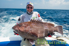 Ein Angler hält einen großen Zackenbarsch auf einem Boot vor der maledivischen Küste. Sonniger Himmel und tiefblaues Meer betonen den aufregenden Angelurlaub. Perfekt für Sport- und Freizeitangler.