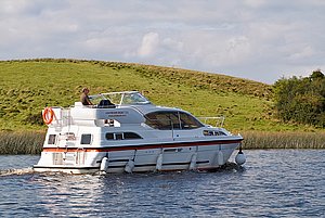 Hausboot auf dem River-Shannon in Irland vor grüner Hügellandschaft gleitend, ideal für Angelurlaub und Erkundungstouren. Perfekt für entspannte Wasserabenteuer und Panorama-Naturlandschaften. Genießen Sie Ruhe und Freiheit auf dem Fluss.