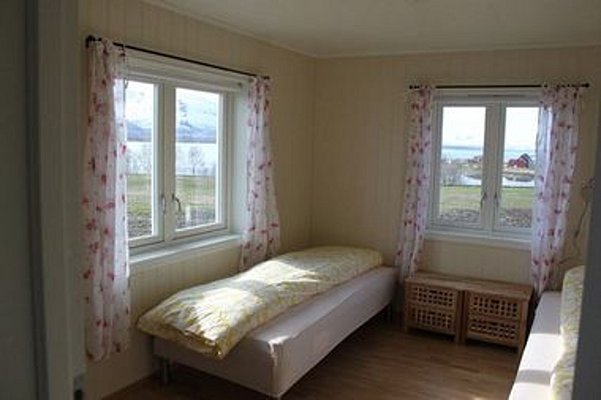 Gemütliches Schlafzimmer in Nord-Norwegen mit zwei Einzelbetten, hellem Holzfußboden und großen Fenstern mit Blick auf die malerische Fjordlandschaft. Ideal für erholsamen Angelurlaub.