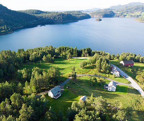 Luftaufnahme von Hitra, Norwegen: Malerische Landschaft mit grünen Wäldern, vereinzelten Häusern und weitem Blick über einen ruhigen See. Ideal für Angelreisen und Naturerlebnisse in unberührter Umgebung.