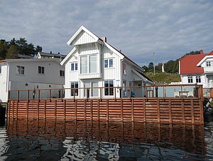 Weißes Haus am Wasser mit Holzterrasse, ideal für Angelreisen. Die ruhige Umgebung bietet perfekte Angelmöglichkeiten und Entspannung. Ideal für einen sorglosen Angelurlaub in natürlicher Umgebung. Abenteuerlust und Erholung vereint.