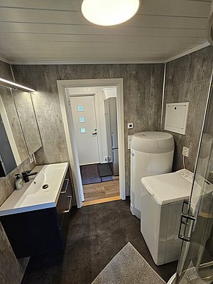 Modernes Badezimmer in Nordland, Norwegen, mit Waschmaschine und Wäschetrockner. Stilvolles Design mit hellen Wänden, Waschbecken und großem Spiegel. Funktionalität trifft auf skandinavische Eleganz. Perfekt für komfortable Angelreisen.
