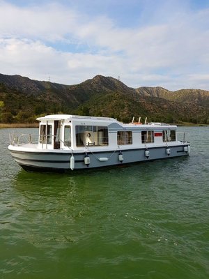 Hausboot auf dem Riba Roja See, Spanien. Umgeben von grünen Hügeln und blauem Himmel, ideal für entspannte Angelurlaube und Abenteuer in der Natur. Perfekte Möglichkeit, das Meeresangeln und die Landschaft zu genießen.