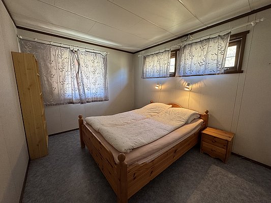 Gemütliches Schlafzimmer mit Holzbett und sanfter Beleuchtung in Hitra, Norwegen. Ideal für entspannte Angelreisen. Lichtdurchfluteter Raum mit Vorhängen für Privatsphäre. Perfekter Rückzugsort nach einem langen Angeltag.