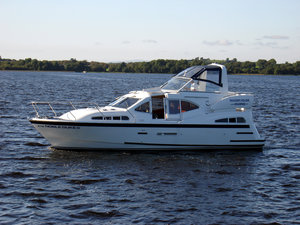 Hausboot auf dem River Erne, Irland, idyllisch vor bewaldetem Ufer. Perfekt für Angelurlaub und entspannende Bootsfahrten. Klare, sonnige Bedingungen schaffen eine einladende Atmosphäre für Freizeit und Abenteuer auf dem Wasser.