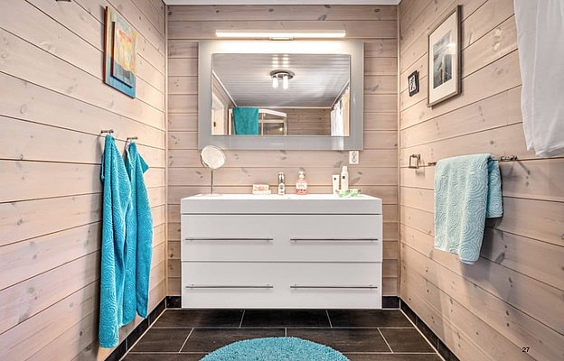 Modernes Badezimmer in Südwest-Norwegen: Holzverkleidung, weiße Waschtischkommode, großer Spiegel und türkise Accessoires sorgen für skandinavisches Flair. Ideal für Angelurlaube, entspannend nach einem langen Tag am Wasser.