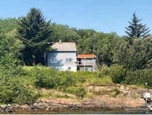 Das Bild zeigt ein weißes Haus in Hitra, Norwegen, umgeben von grünen Bäumen vor einer felsigen Küste. Perfekte Kulisse für einen entspannten Angelurlaub in skandinavischer Naturidylle.